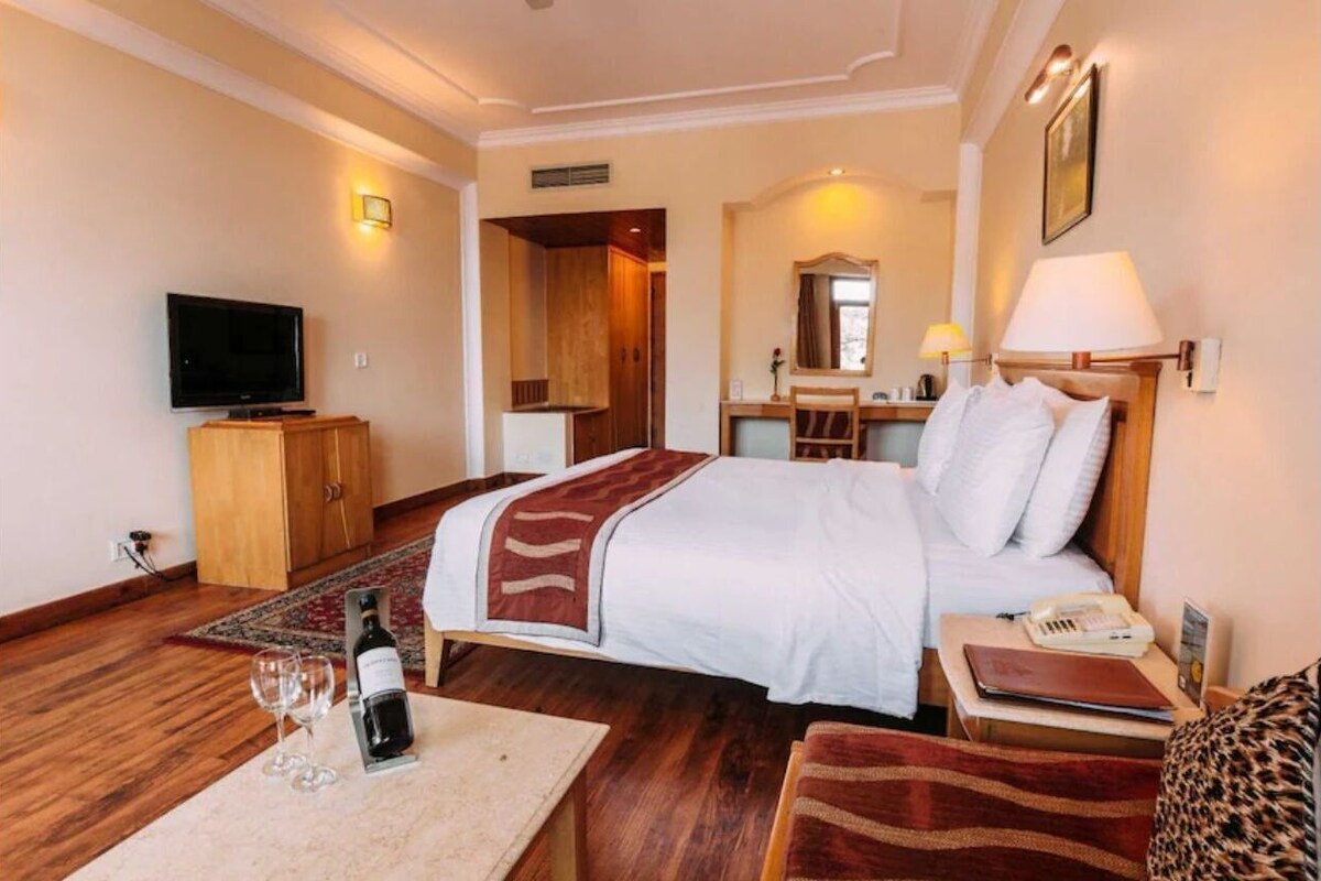 A hotel room with a bed, a television, a desk with a lamp, a mirror, and a window.