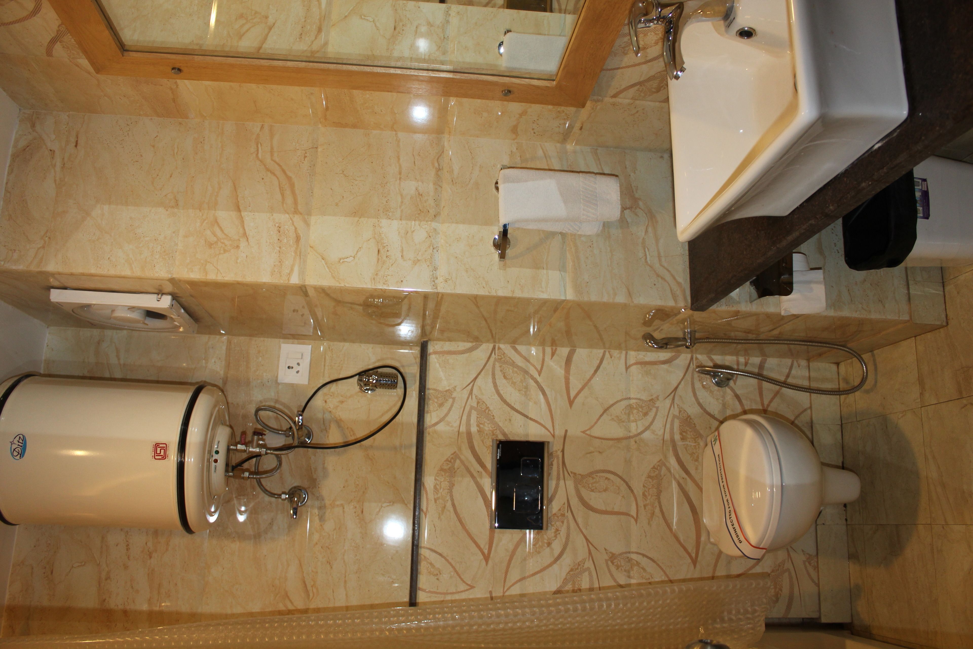 A bathroom with a marble floor, a white sink, a mirror, a towel dispenser, and a toilet.