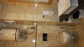 A bathroom with a marble floor, a white sink, a mirror, a towel dispenser, and a toilet.
