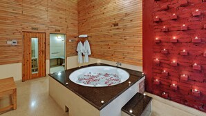 A spa room with a large bathtub, wooden walls, a red brick wall with candles, and a mirror. - Bravia Hotel Manali Inn (Manali)