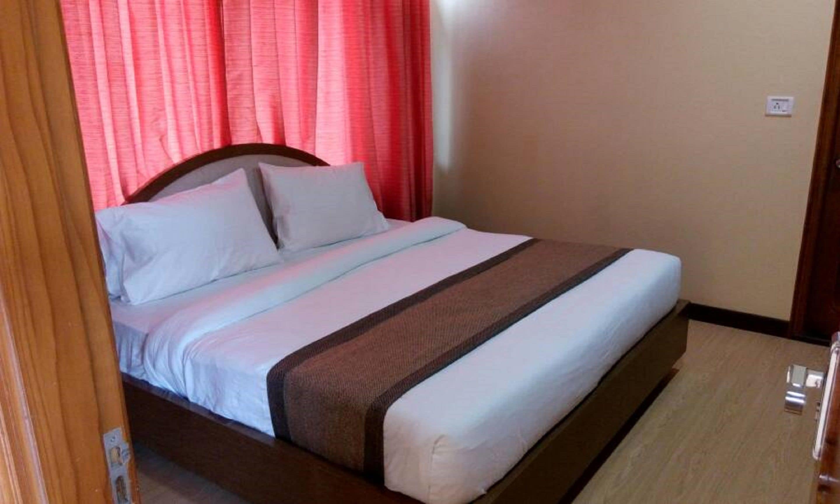 Une chambre d’hôtel standard, avec un lit, des rideaux et une porte en bois.
