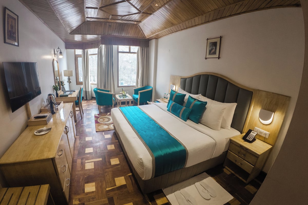 A hotel room with a large bed, a desk, a chair, a TV, and a window with curtains.