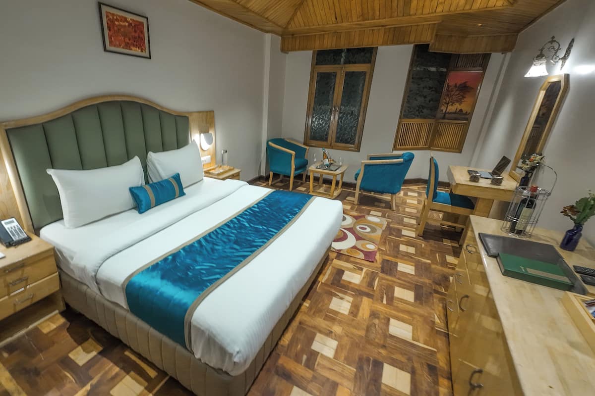 A hotel room with a large bed, a desk, a chair, and a small table.