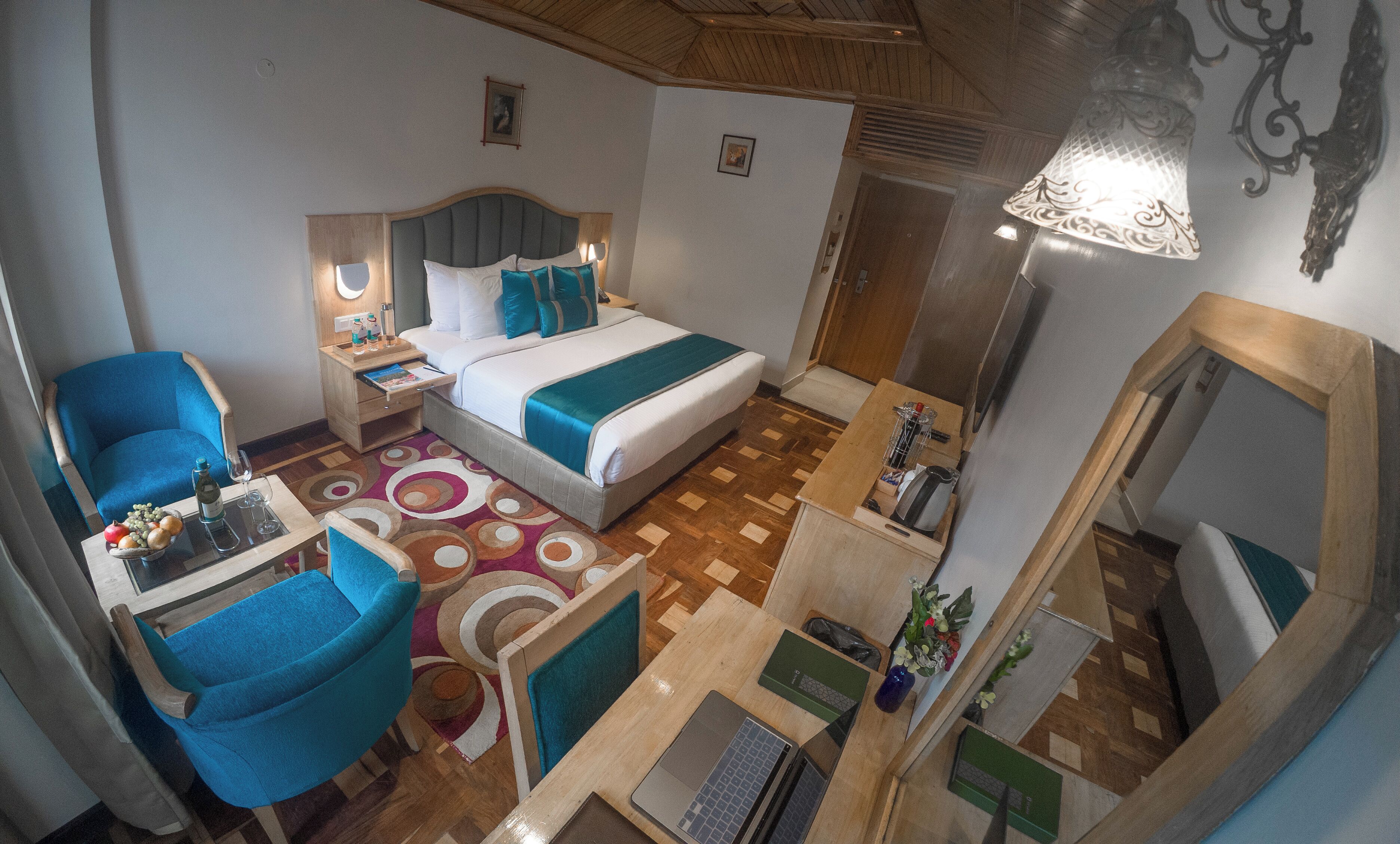 Habitación de hotel con cama, escritorio con laptop, silla, mesita de noche con lámpara y espejo.