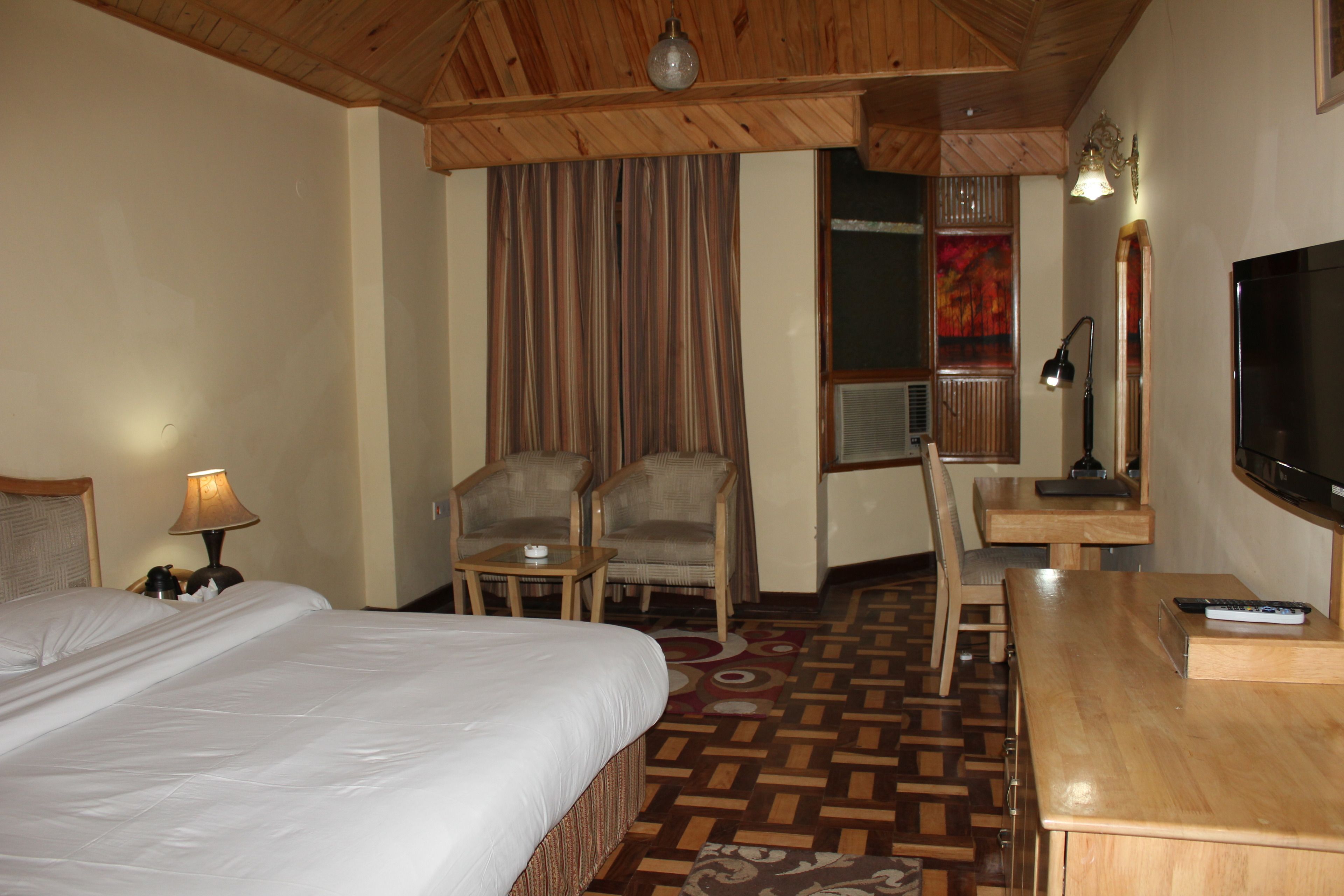 A hotel room with a bed, two armchairs, a small table, a desk with a TV, and a lamp.