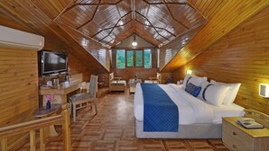 A cozy, wooden cabin bedroom with a large bed, a desk with a TV, and a view of the forest through the windows. - Bravia Hotel Manali Inn (Manali)