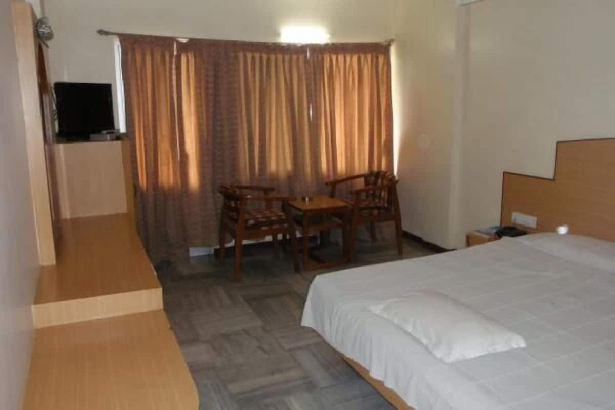 Una habitación de hotel con una cama, una mesita con sillas, un televisor y cortinas.