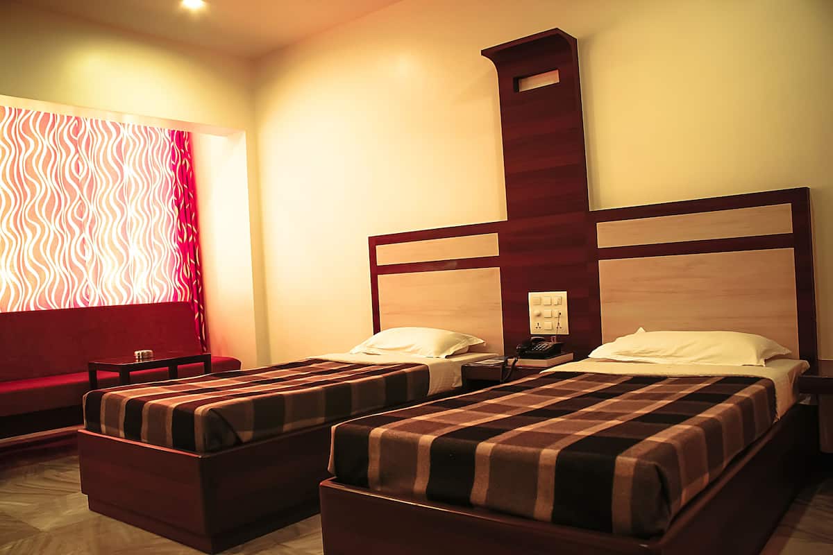 Habitación de hotel con dos camas individuales, un sofá, una mesita pequeña y una mesita de noche con lámpara.