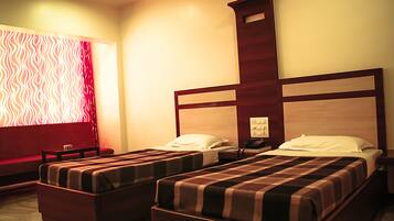 Habitación de hotel con dos camas individuales, un sofá, una mesita pequeña y una mesita de noche con lámpara.