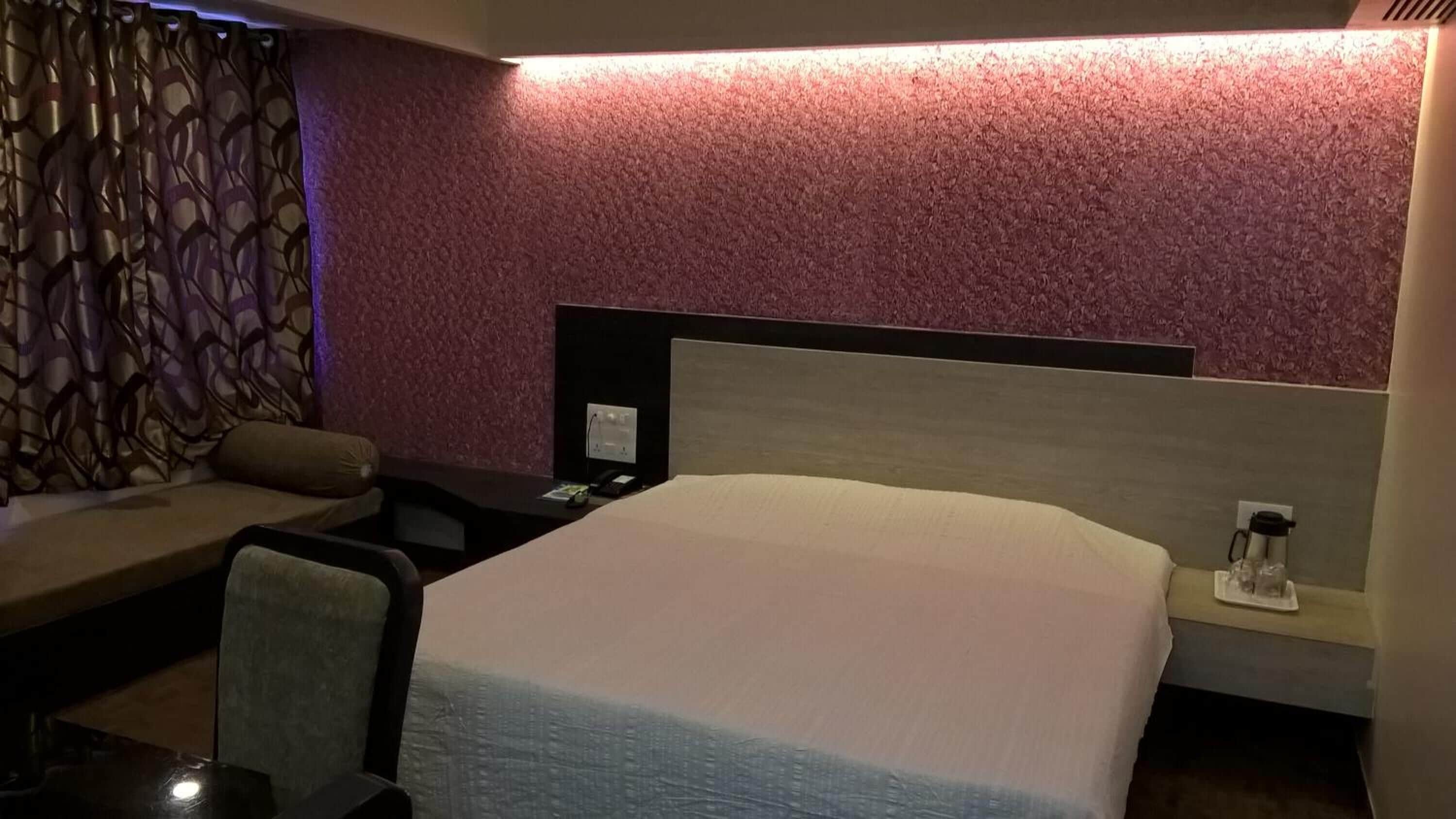 Habitación de hotel con una cama grande, una mesita de noche con lámpara, una zona de estar con sofá y sillón, y una pared decorada.