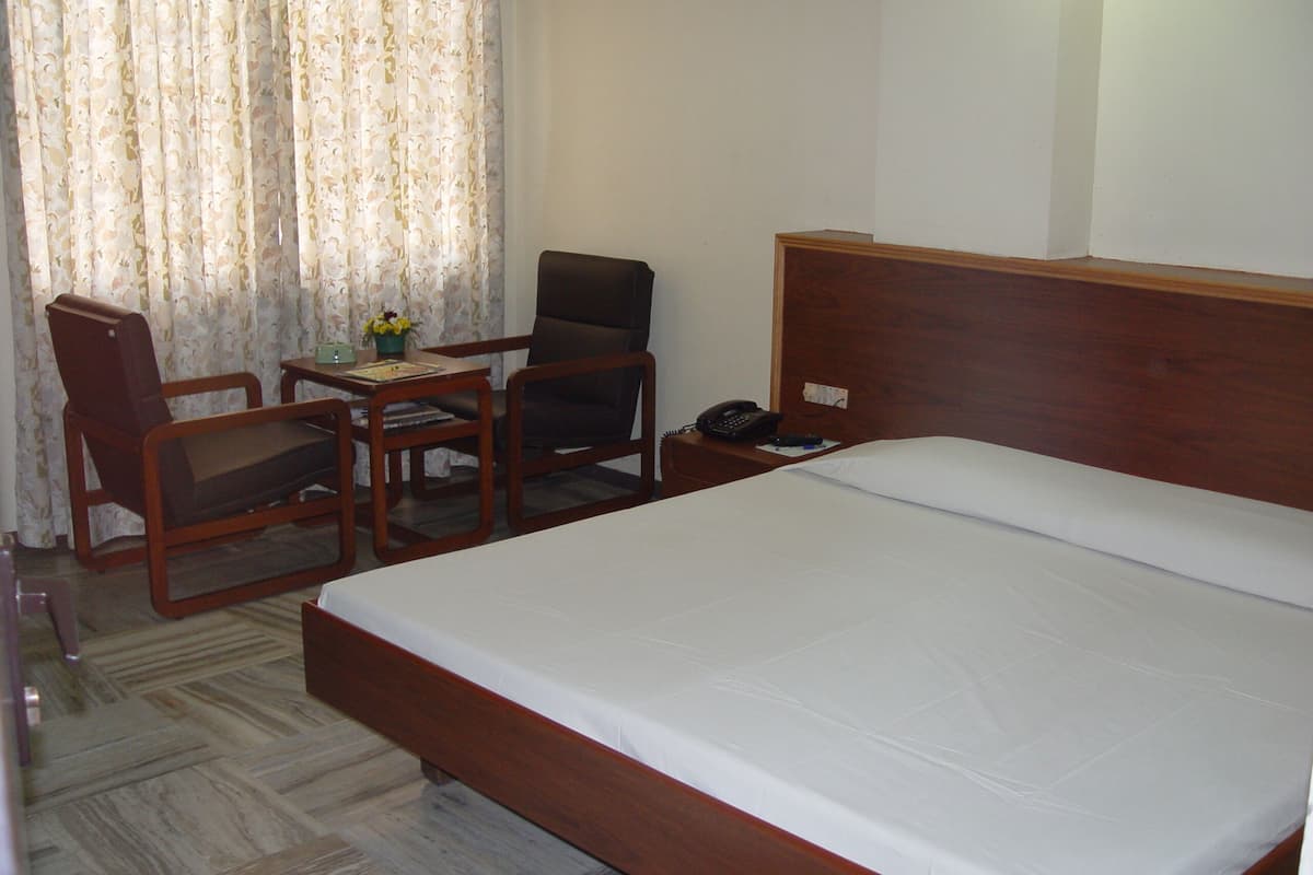 Habitación de hotel con cama de madera, un escritorio con silla, un teléfono y una ventana con cortinas.