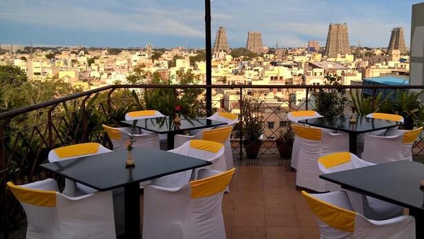 A terrace with tables and chairs, overlooking a cityscape with distinctive temple-like structures. - Hotel Supreme (Madurai)