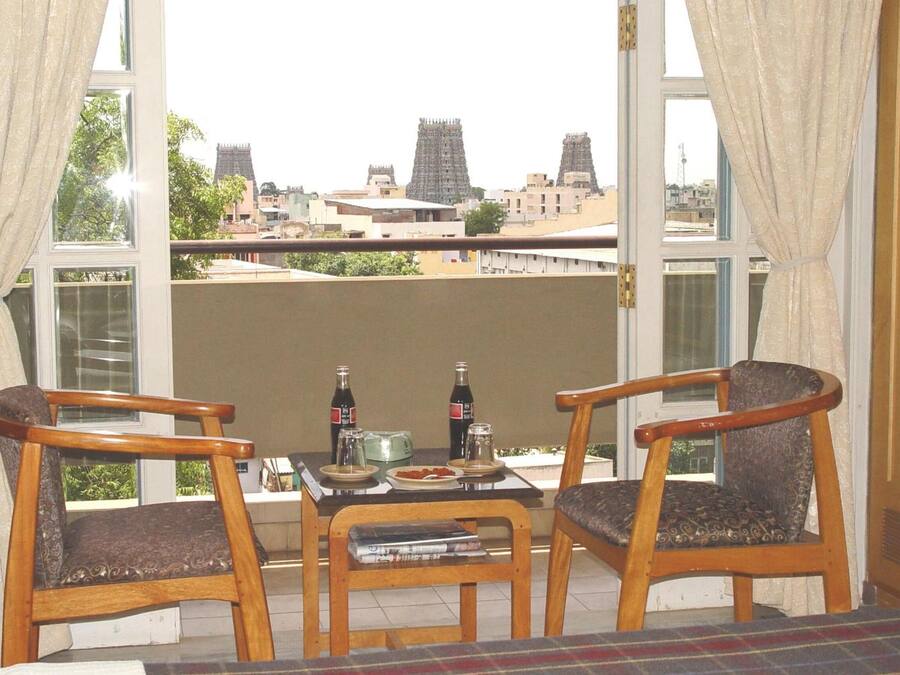 Un balcón con dos sillas de madera, una mesita con botellas, un tostador y un bol de fruta.