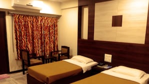 A hotel room with two single beds, a small desk, a chair, and a patterned curtain. - Hotel Supreme (Madurai)