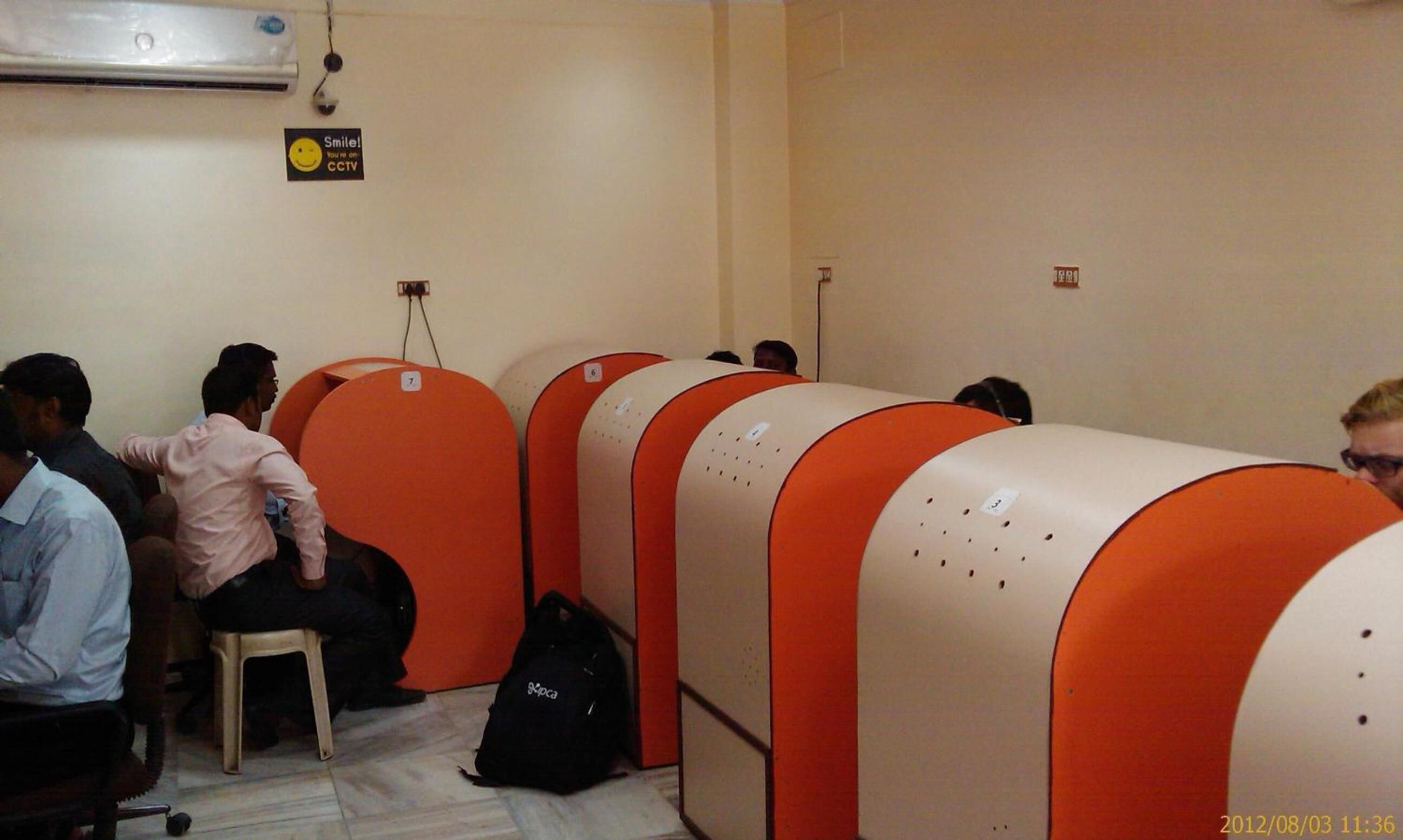 A waiting area with orange and white seating, a CCTV sign, and a wall-mounted air conditioner.