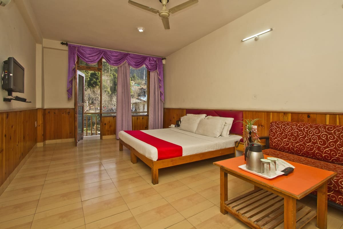 A bedroom with a bed, a sofa, a table with a kettle, and a TV on the wall.