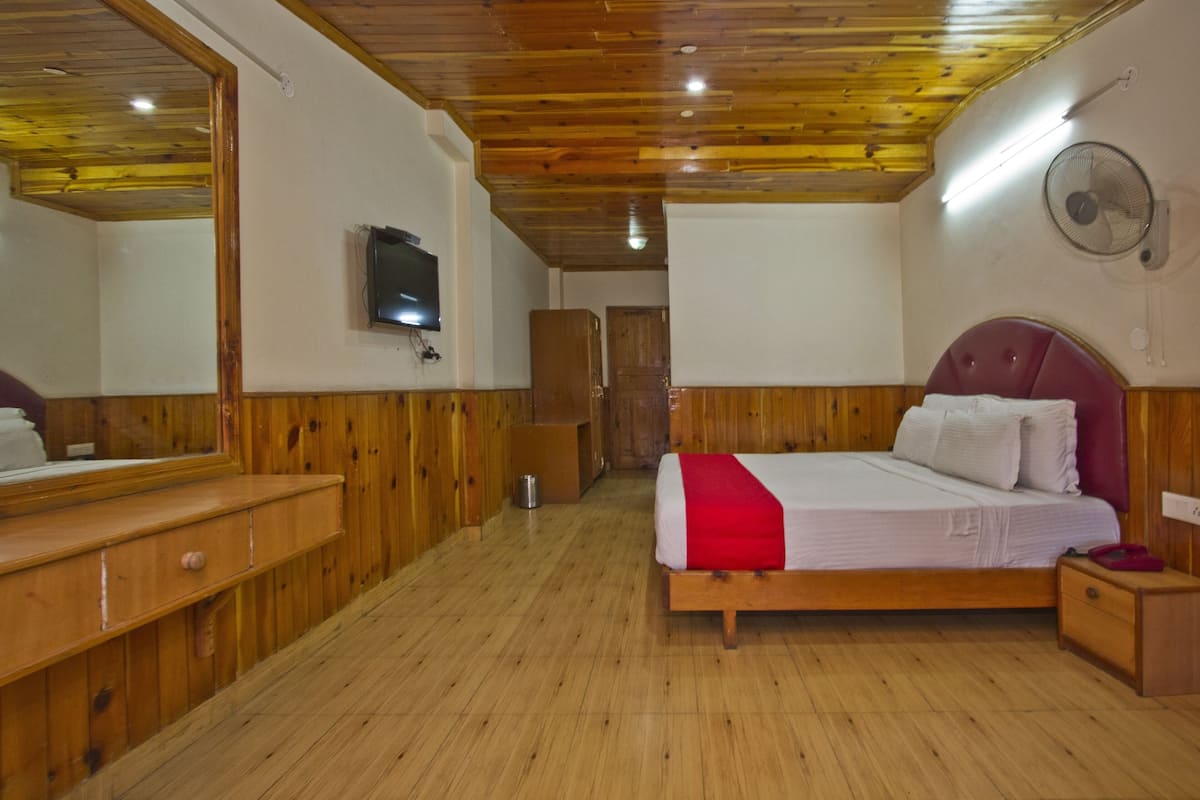 A wooden-paneled bedroom with a bed, a dresser, a mirror, a television, and a fan.