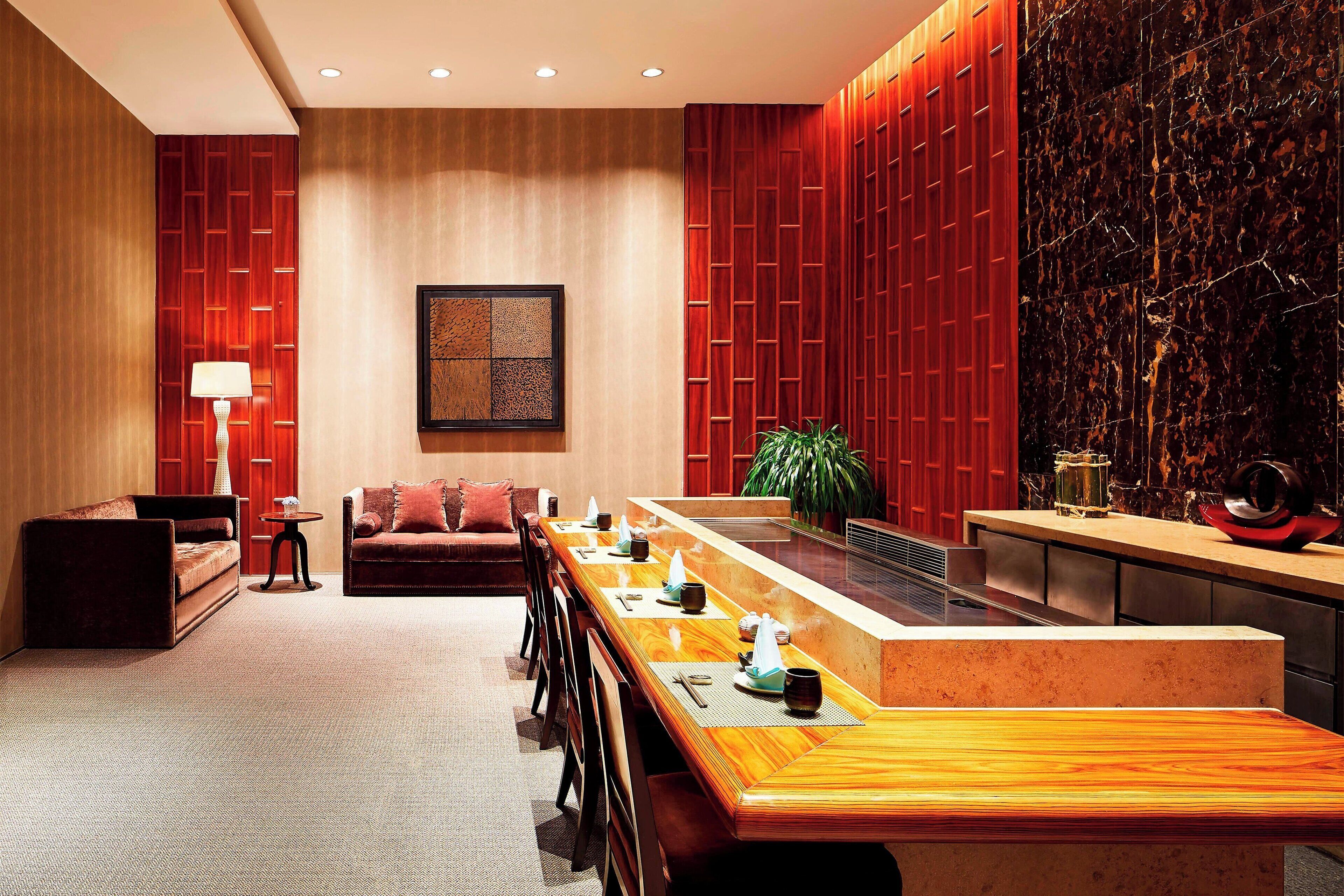 A modern hotel lobby with a long reception desk, seating area, and a large plant.