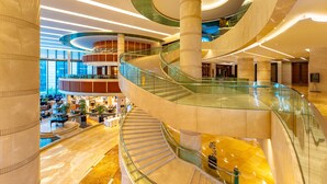 A multi-level atrium with glass railings, marble flooring, and a central staircase.