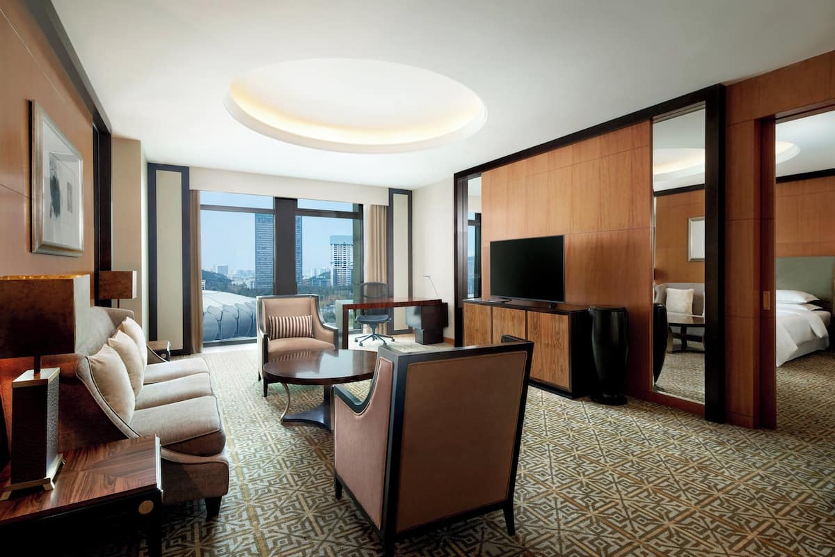 A hotel room with a sofa, armchair, desk, television, and a bed.