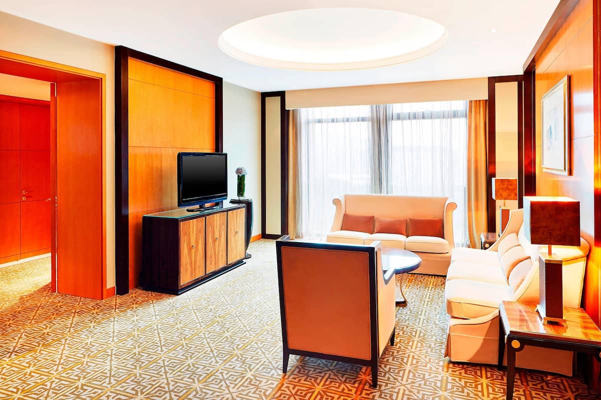 A hotel room with a sofa, armchairs, a TV, a cabinet, and a patterned floor.