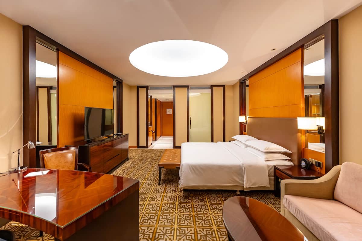 A hotel room with a large bed, a desk, a TV, a sofa, and a mirror.