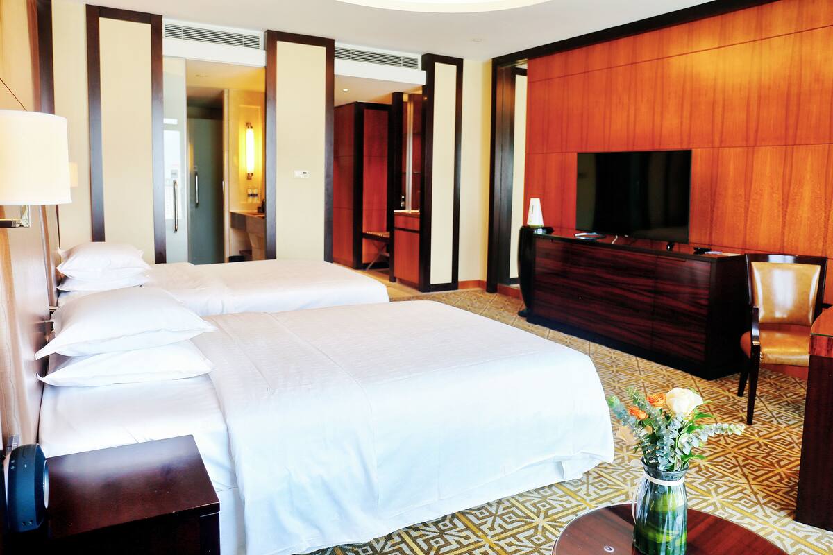 A hotel room with a large bed, a desk, a TV, and a vase of flowers.