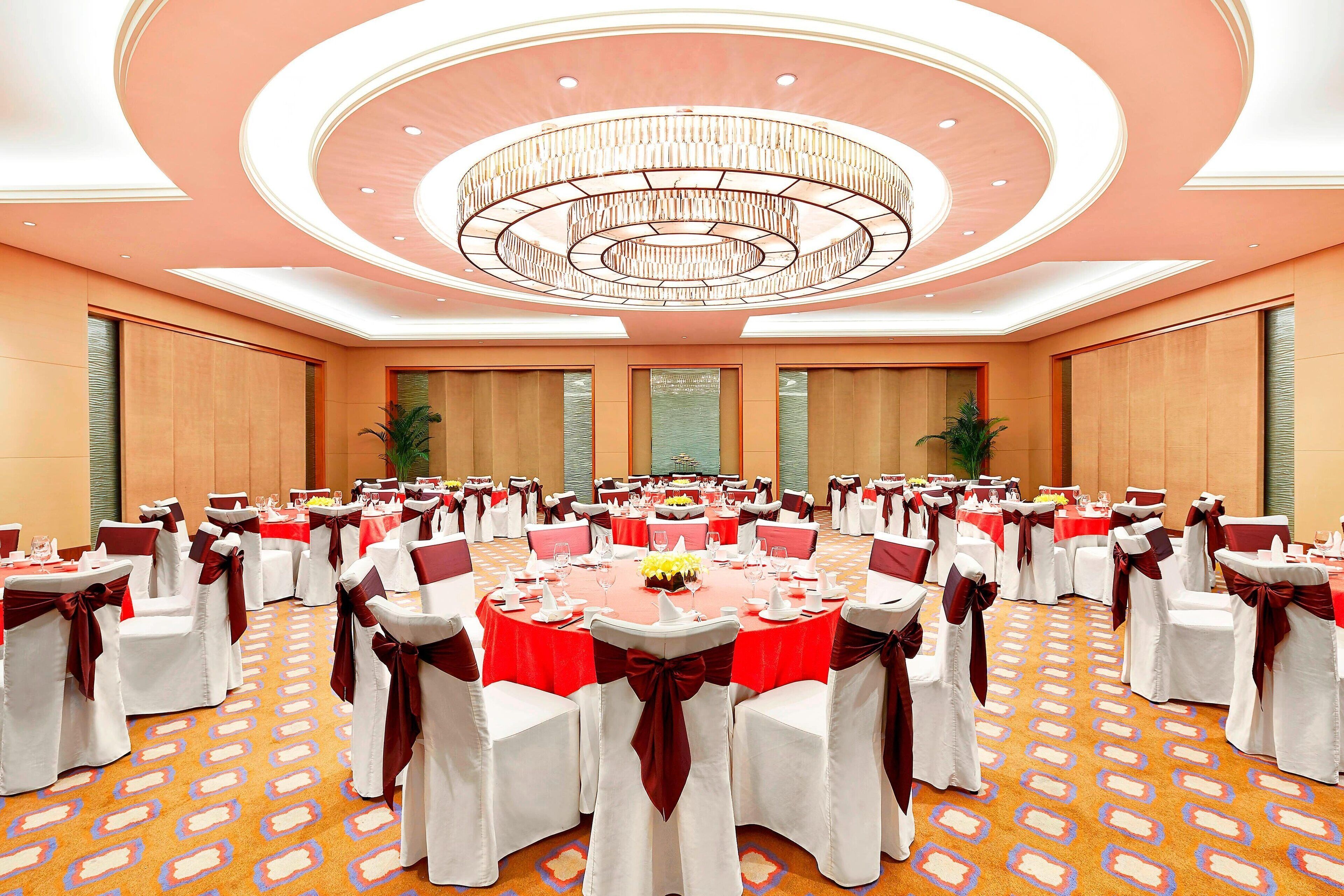 Une salle de banquet avec des tables rondes, des chaises blanches et des nappes rouges.