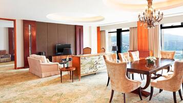 A hotel room with a dining area, a sofa, a TV, and a view of the city.
