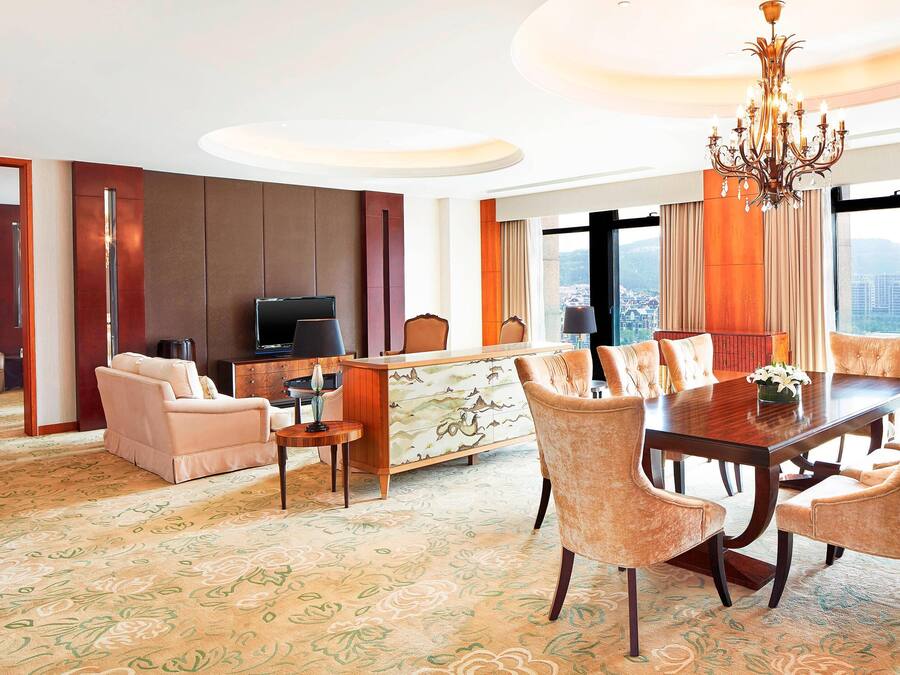 A hotel room with a dining area, a sofa, a TV, and a view of the city.