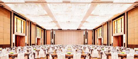Une vaste salle de banquet, avec des rangées de tables rondes, chacune recouverte d’une nappe blanche et entourée de chaises, et un sol recouvert de moquette.