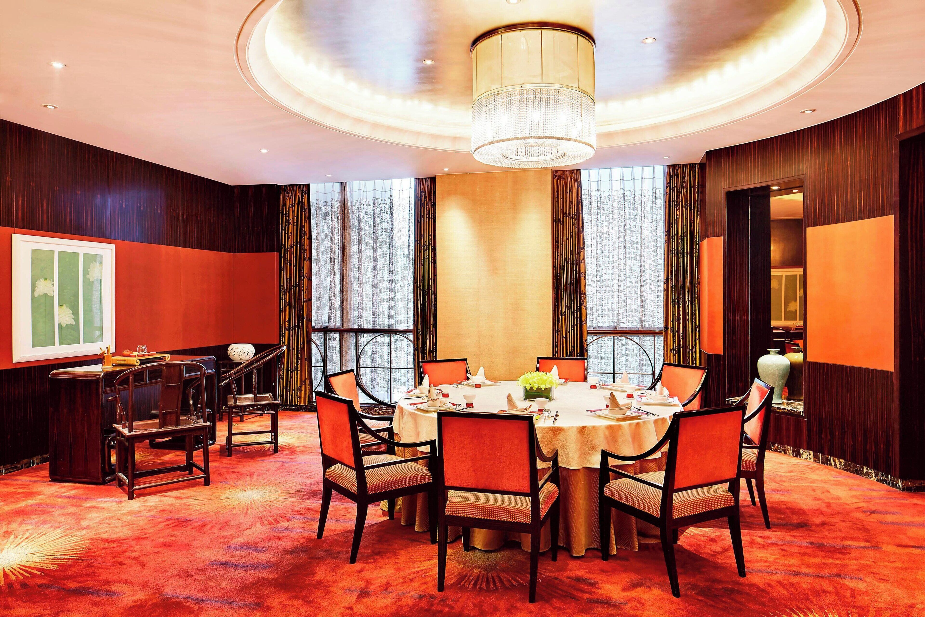 A conference room with a round table, chairs, a chandelier, and large windows.