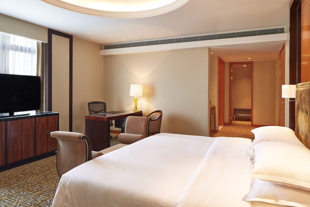 A hotel room with a large bed, a TV, a desk with a chair, and a lamp.