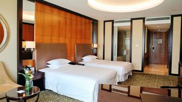 A hotel room with two beds, a sitting area with a table and a chair, a mirror, and a large mirror on the wall.