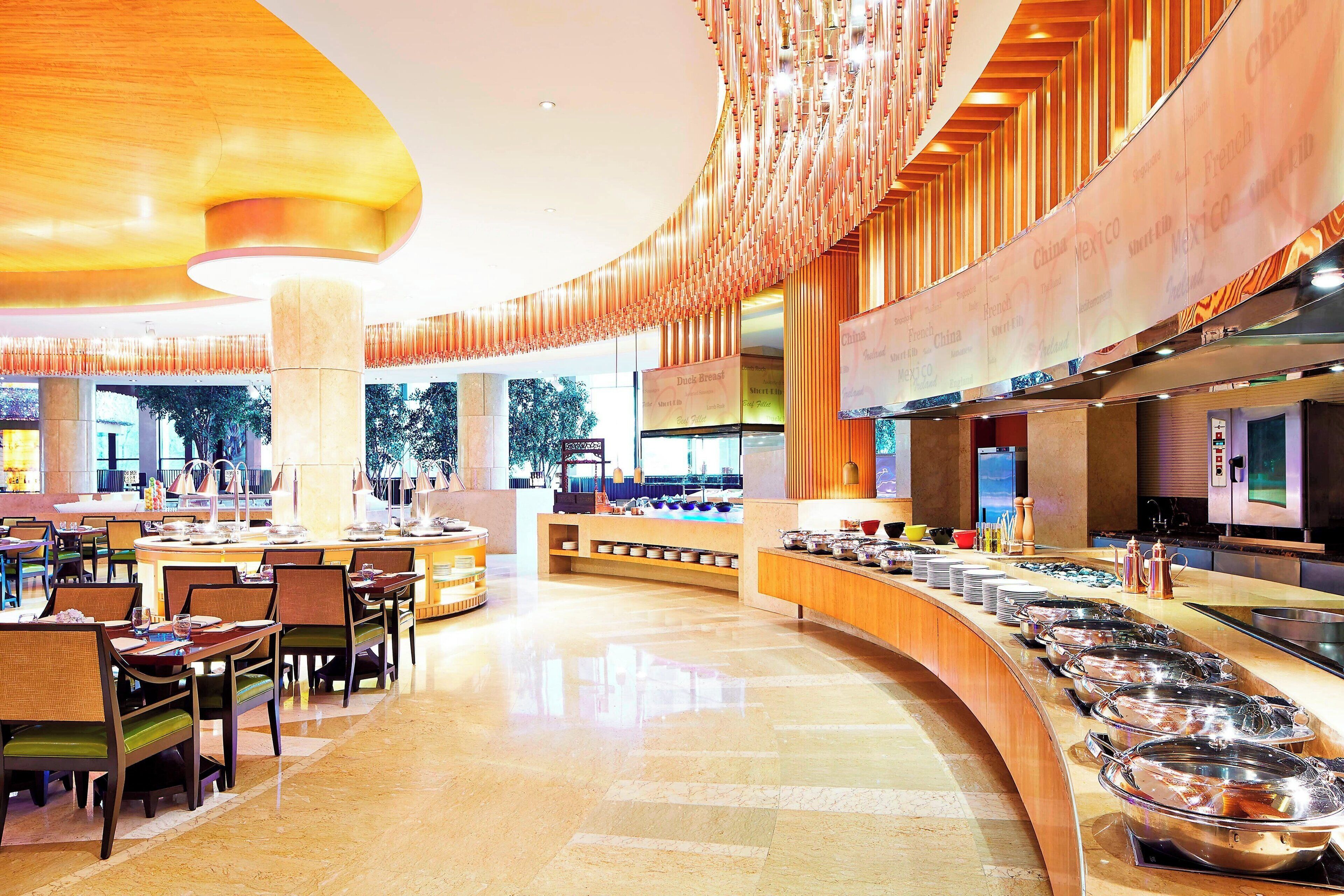 A modern hotel lobby with a curved reception desk, buffet area with food containers, and seating arrangements.