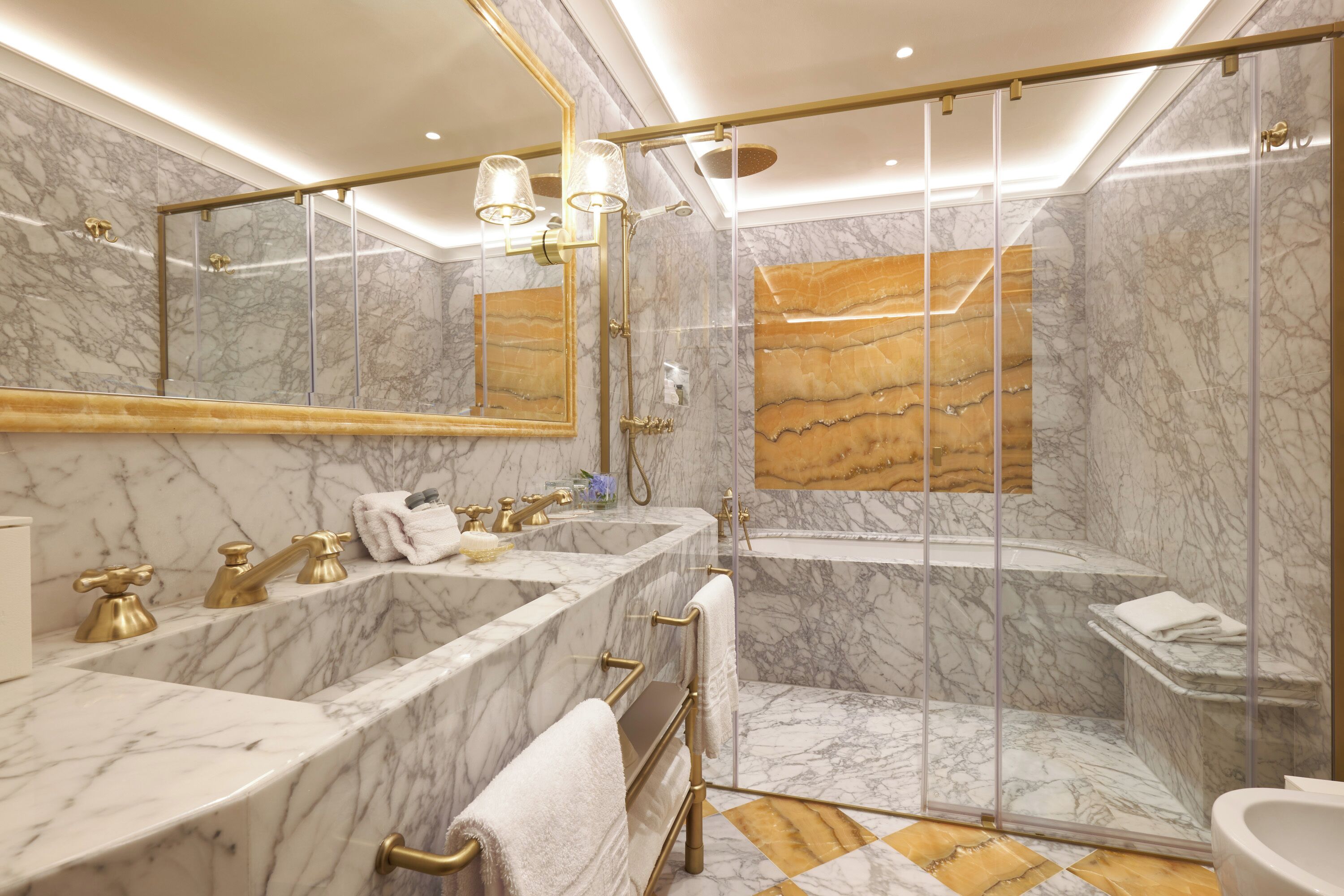 Ein luxuriöses Badezimmer mit Marmorwänden, einem großen Spiegel, zwei Waschbecken, einer Badewanne und einer Duschkabine.