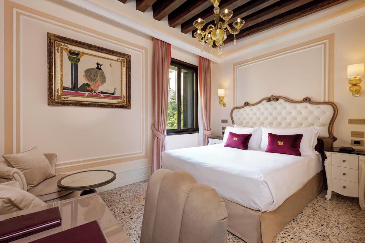 Habitación de hotel con una cama grande, una mesa redonda, una silla, una araña y un cuadro en la pared.