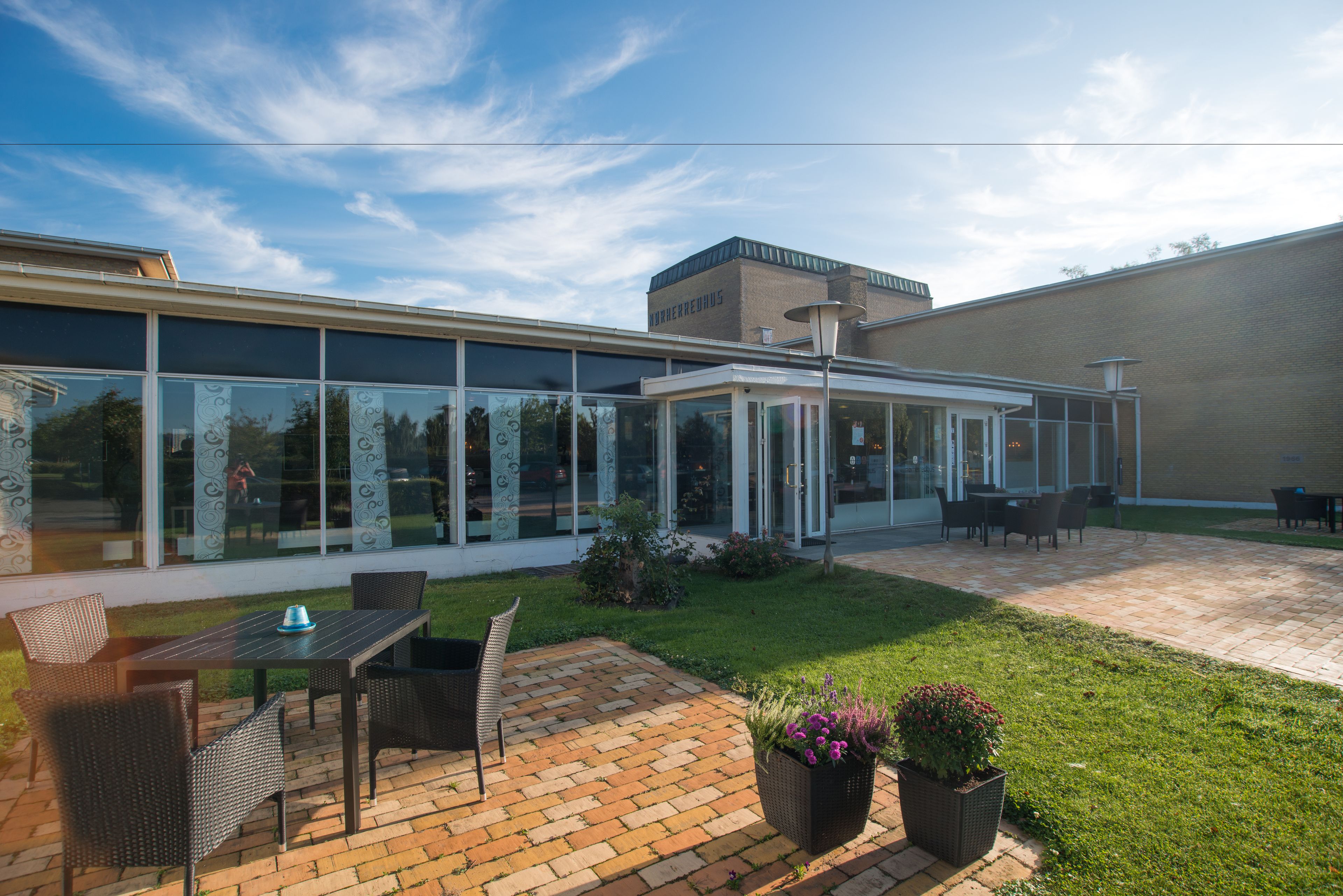 A modern building with a glass extension, outdoor seating, and a brick patio.
