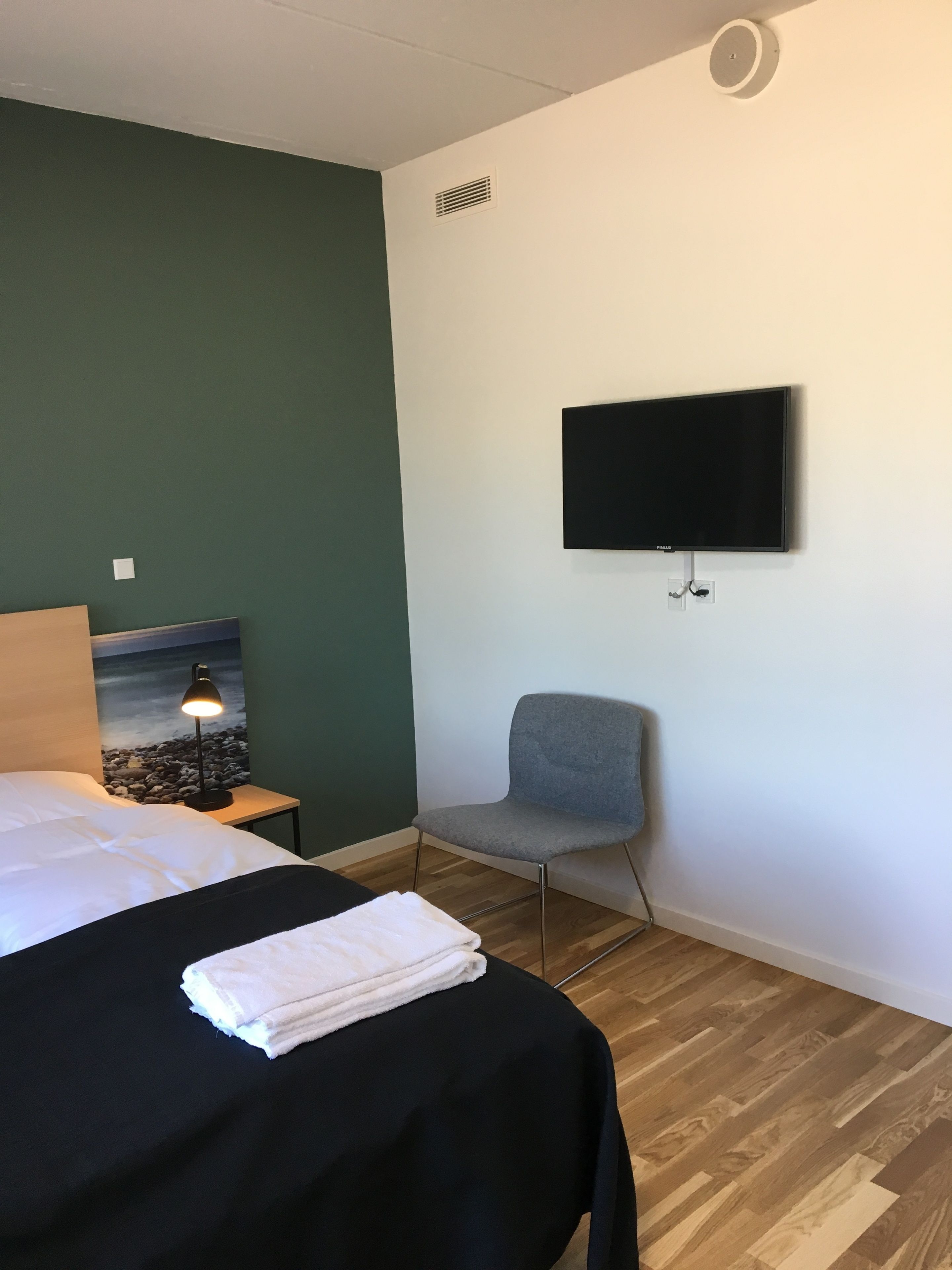 Hotelkamer met een bed, een stoel, een bureau met lamp, een flatscreen televisie aan de muur en een schilderij.