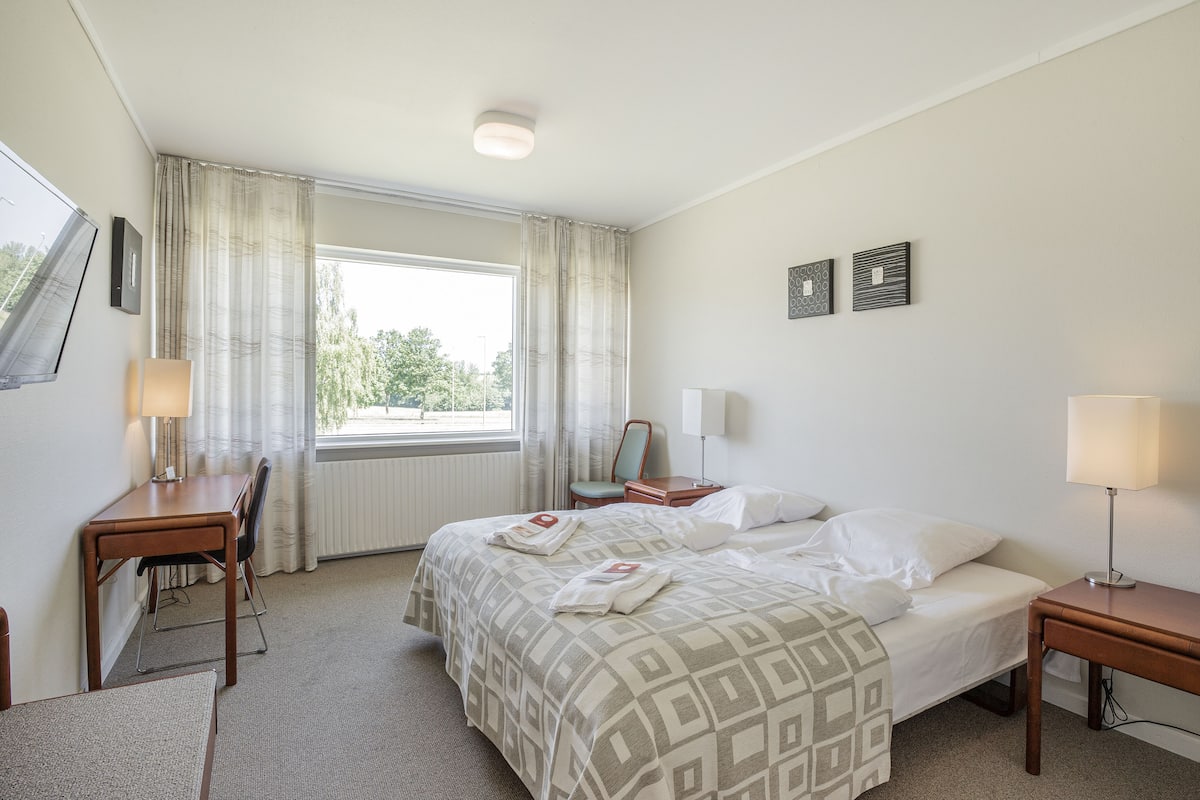 Une chambre d’hôtel avec un lit, des tables de chevet, un bureau et une chaise.