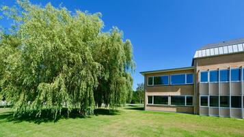 A modern building with a brick facade and large windows, surrounded by a well-maintained lawn and a large tree.