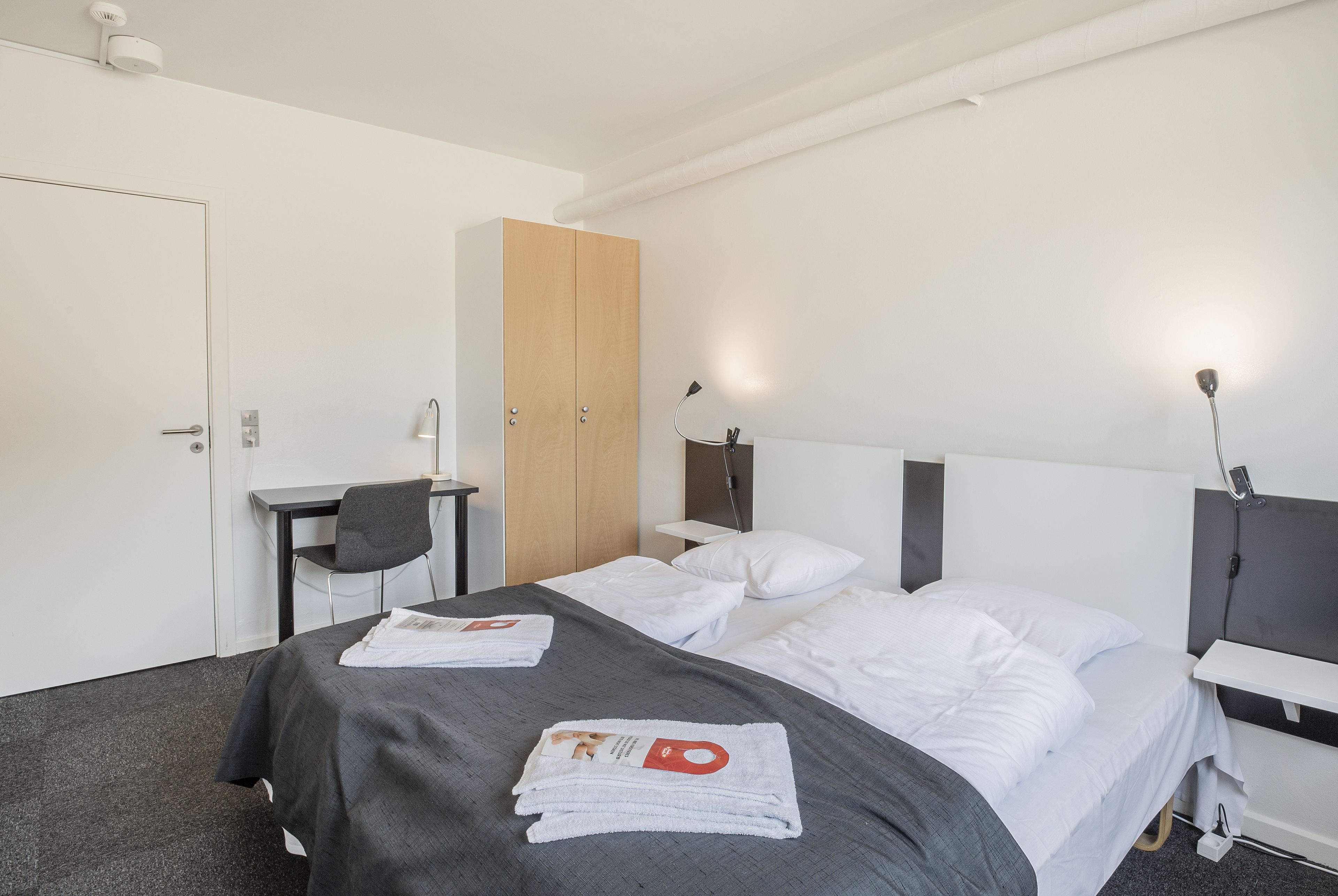 A modern hotel room with a bed, a desk, and a wardrobe.