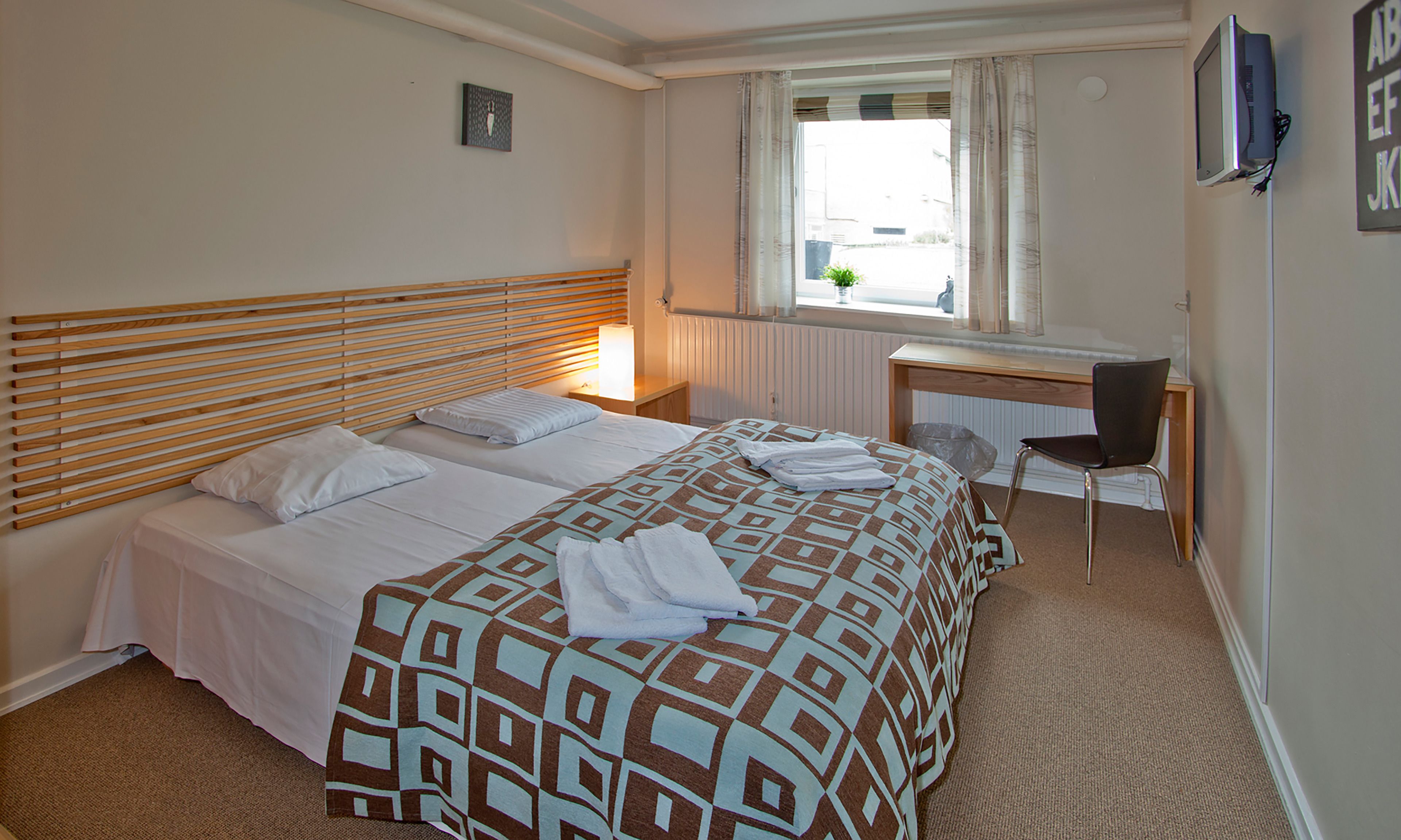A hotel room with a bed, a desk, a chair, and a window with curtains.