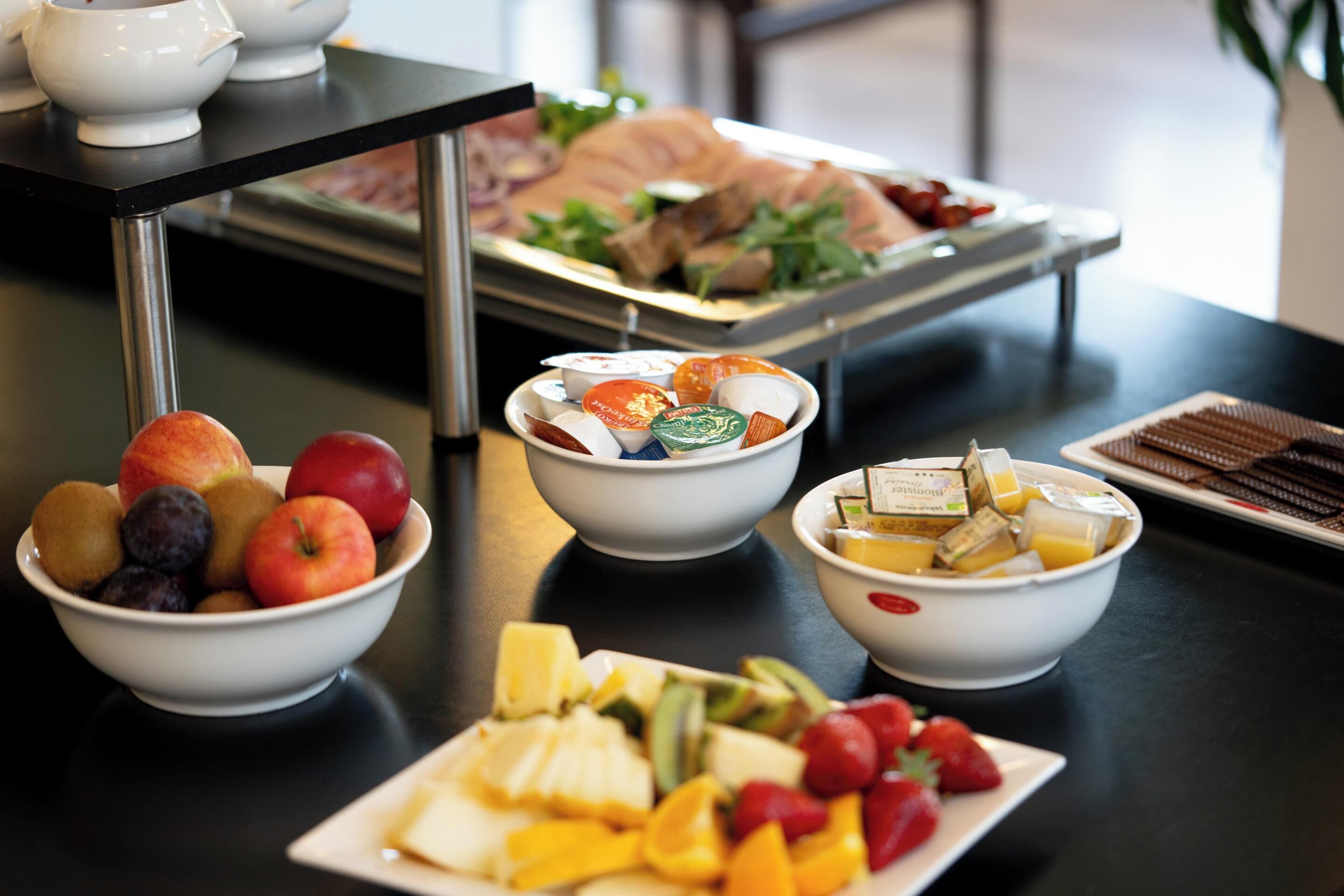 Une table de buffet proposant une variété d’aliments, notamment des fruits, des fromages et des pâtisseries.