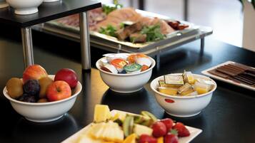 Une table de buffet proposant une variété d’aliments, notamment des fruits, des fromages et des pâtisseries.