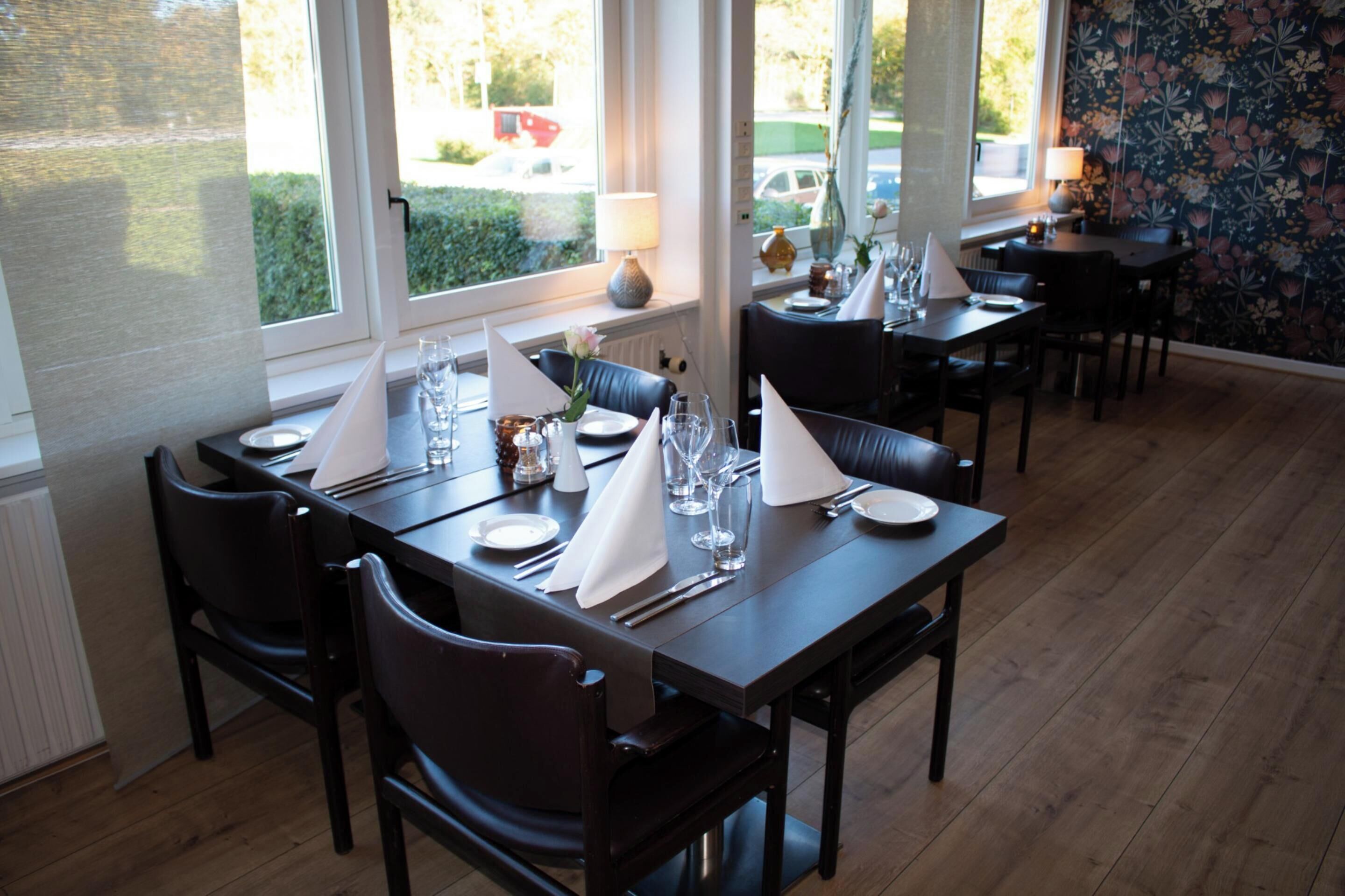 A dining area with a long table set for a meal, chairs, and a window with a view of the outside.
