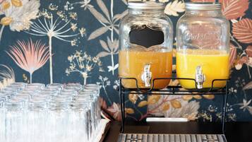Una estación de bebidas con dos dispensadores de vidrio llenos de jugo de naranja, una bandeja de vasos vacíos y un teclado sobre una mesa.