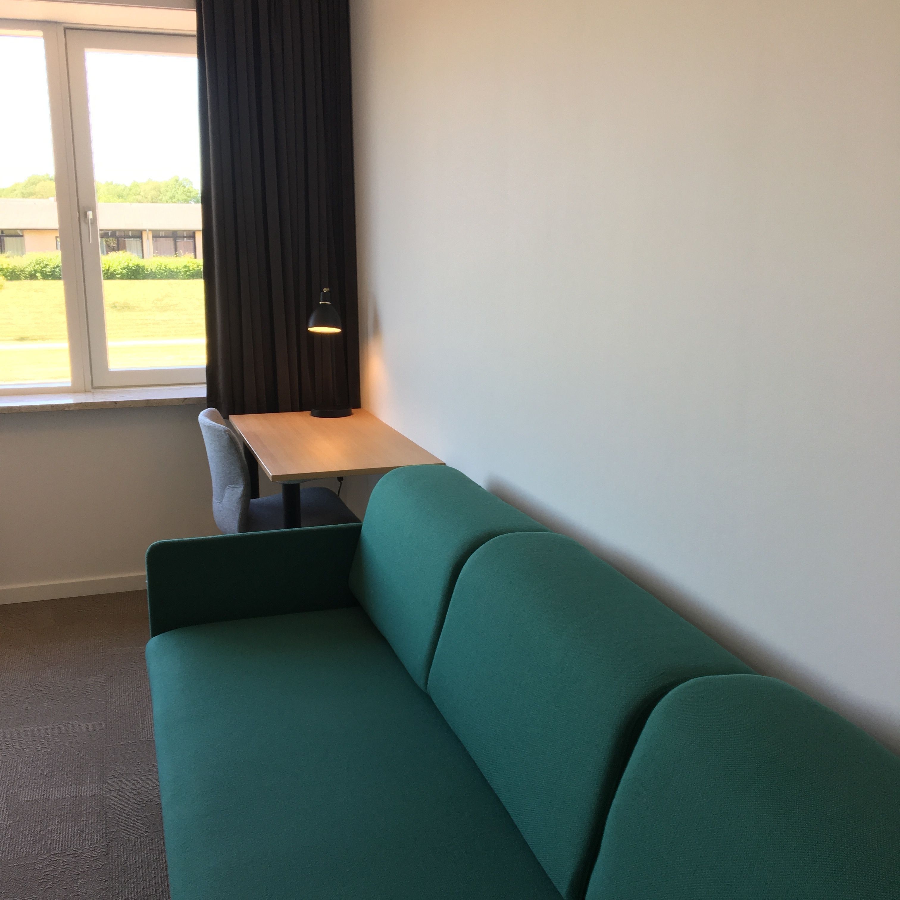 Een kamer met een groene bank, een klein tafeltje en een raam met gordijnen.