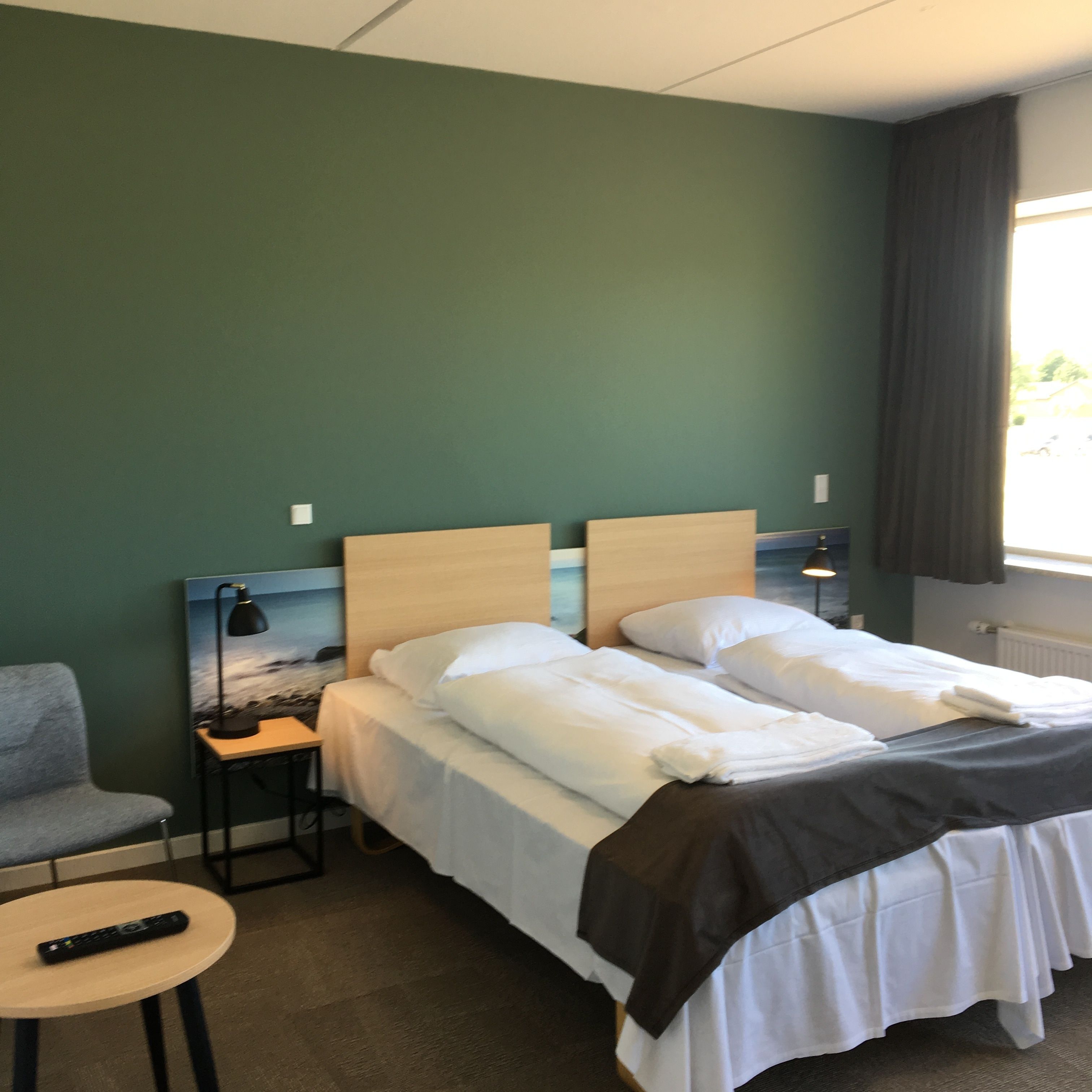A hotel room with a bed, a chair, a small table, and a painting on the wall.