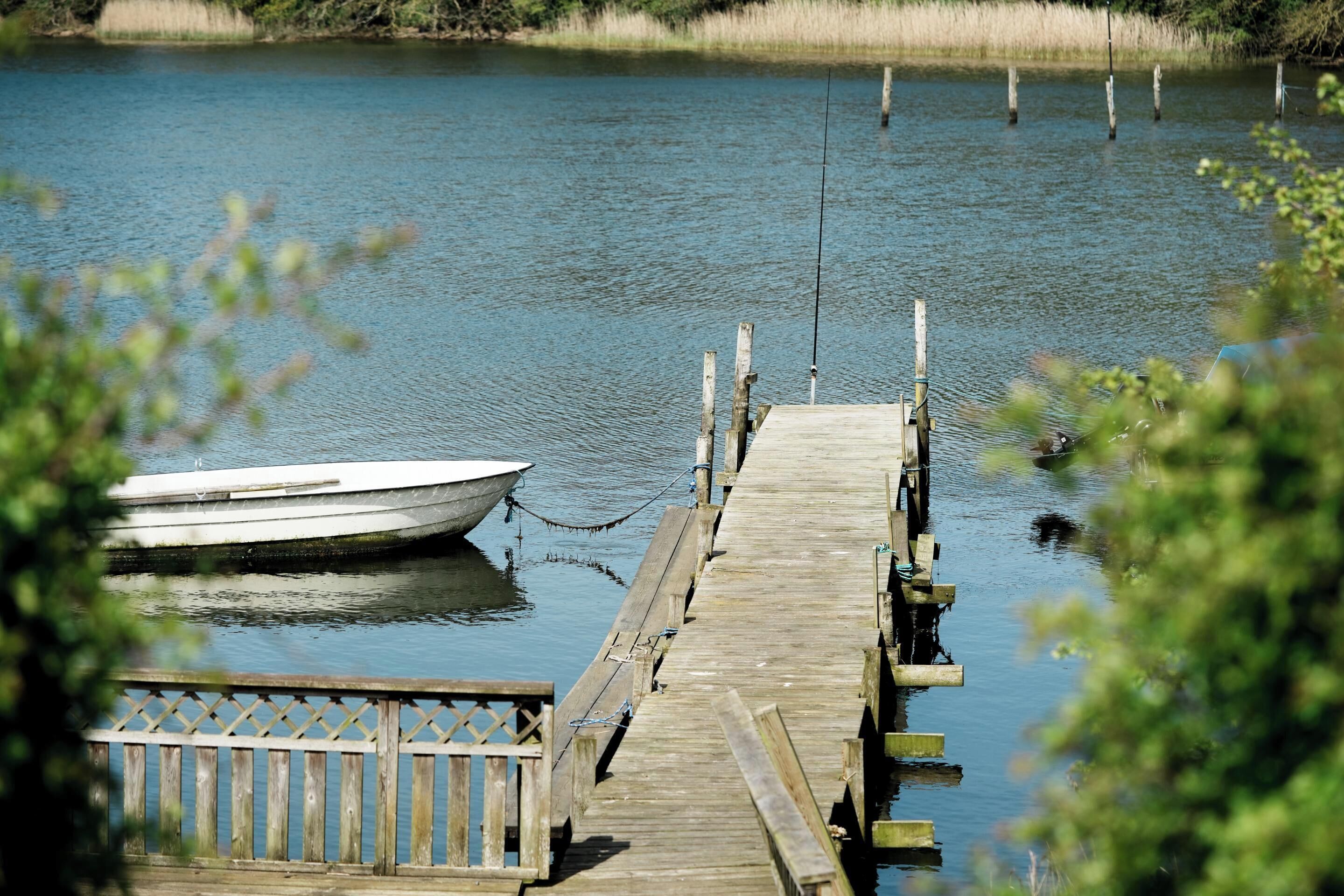 Ein hölzerner Steg erstreckt sich über einen stillen See, am Ende ist ein Boot festgemacht.